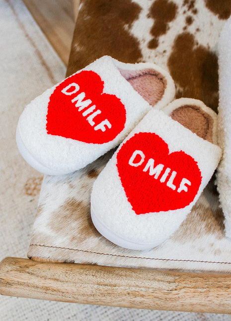 White slippers with red hearts and 'DMILF' text on a brown and white surface.